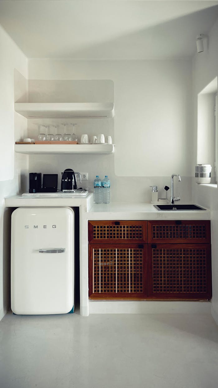 Fragment of interior of kitchen with white walls and floor furnished with minimalist shelves and cupboard sink and fridge